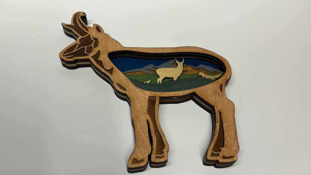 Wooden antelope shaped ornament with a landscape inset on a white background