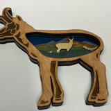Wooden antelope shaped ornament with a landscape inset on a white background