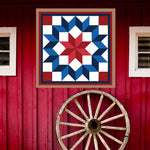 Carpenter Barn Quilt Pattern displayed on a rustic red barn with a vintage wagon wheel, showing the finished painted barn quilt outdoors.