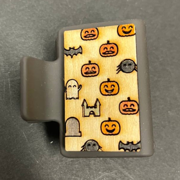 A small hair claw clip with hand-painted wood design featuring pumpkins, ghosts, bats, and spiders for a Halloween aesthetic.