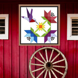 Hummingbird Barn Quilt Pattern displayed on a rustic red barn with a vintage wagon wheel, showing the finished painted barn quilt outdoors.