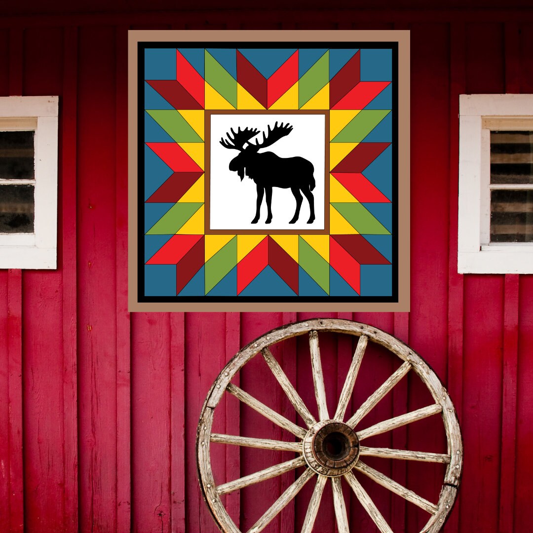 Moose in the wild Barn Quilt Pattern displayed on a rustic red barn with a vintage wagon wheel, showing the finished painted barn quilt outdoors.