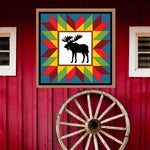 Moose in the wild Barn Quilt Pattern displayed on a rustic red barn with a vintage wagon wheel, showing the finished painted barn quilt outdoors.