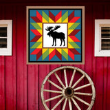 Moose in the wild Barn Quilt Pattern displayed on a rustic red barn with a vintage wagon wheel, showing the finished painted barn quilt outdoors.