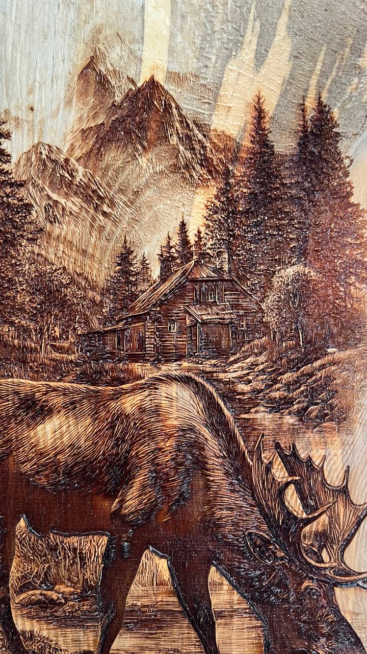 Wooden carving of a moose, cabin, and mountain landscape