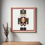 Nutcracker Christmas barn quilt pattern featuring a geometric holiday nutcracker in forest green, burgundy, blush pink, gold, cream and black. Printable DIY barn quilt design for painted wood signs, farmhouse Christmas decor, holiday wall art, porch decorations and handmade seasonal projects.
