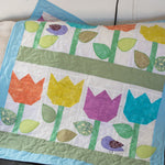 A mini quilt wall hanging featuring a pattern of tulips in various colors with leaves and a bird motif, appliquéd in a quilted fabric.