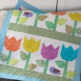 A mini quilt wall hanging featuring a pattern of tulips in various colors with leaves and a bird motif, appliquéd in a quilted fabric.