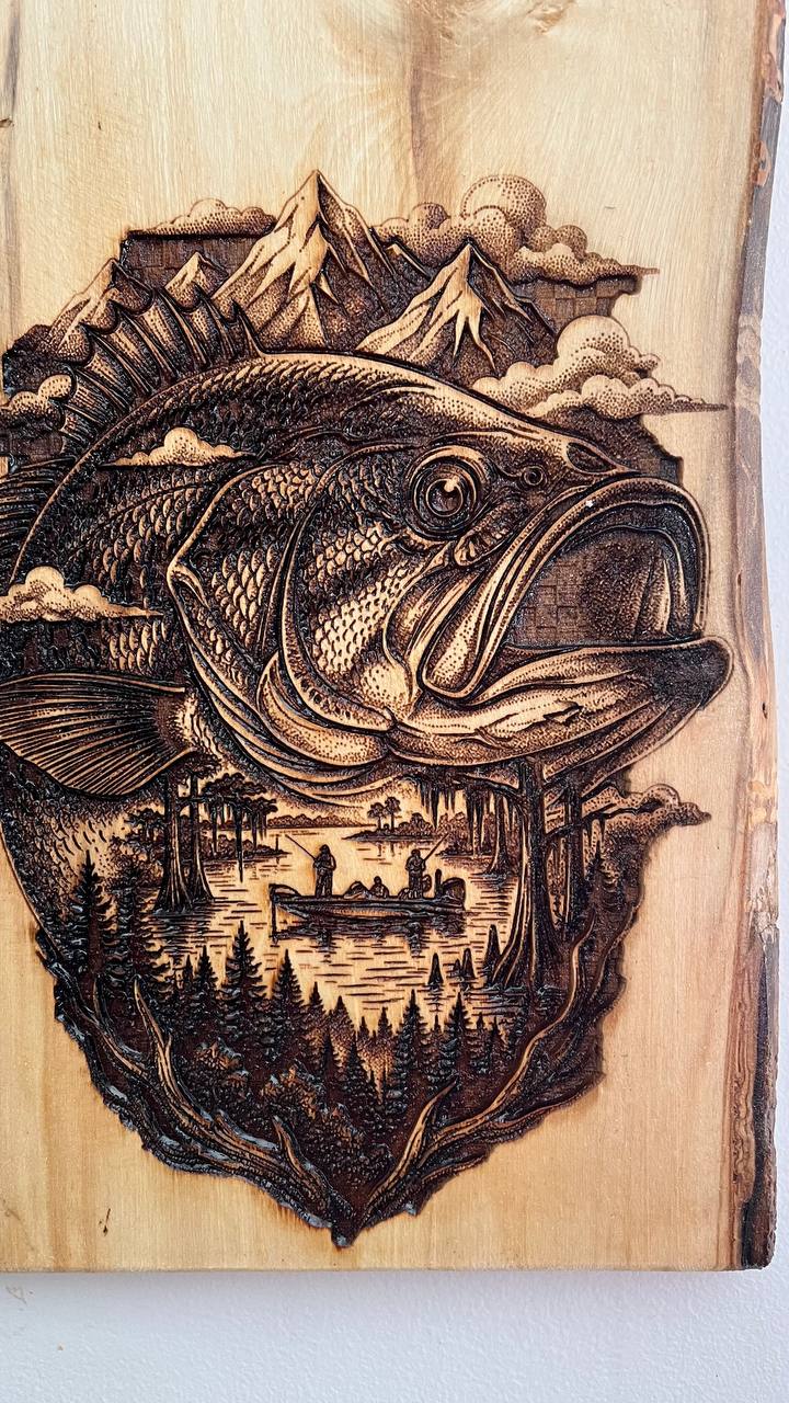 Wooden plaque with a detailed engraving of a fish, trees, and mountains.