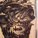 Wooden plaque with a detailed engraving of a fish, trees, and mountains.