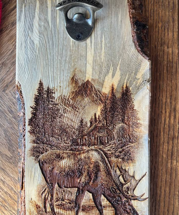 Wooden bottle opener with engraved scene of a deer and mountains on a wooden background