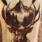 Wooden plaque with a deer head and antlers design, featuring a mountain and trees in the background.