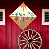 Veggie Garden Barn Quilt Pattern displayed on a rustic red barn with a vintage wagon wheel, showing the finished painted barn quilt outdoors.