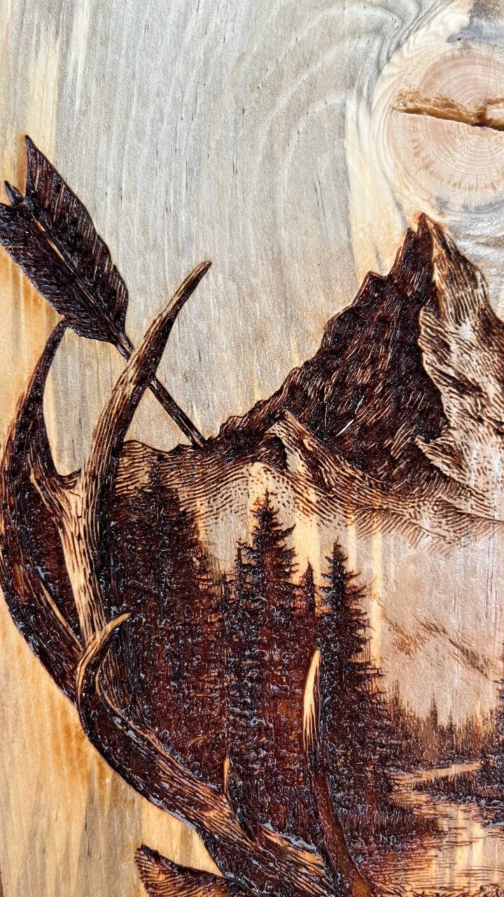 Wooden carving of a mountain landscape with trees and a bird.