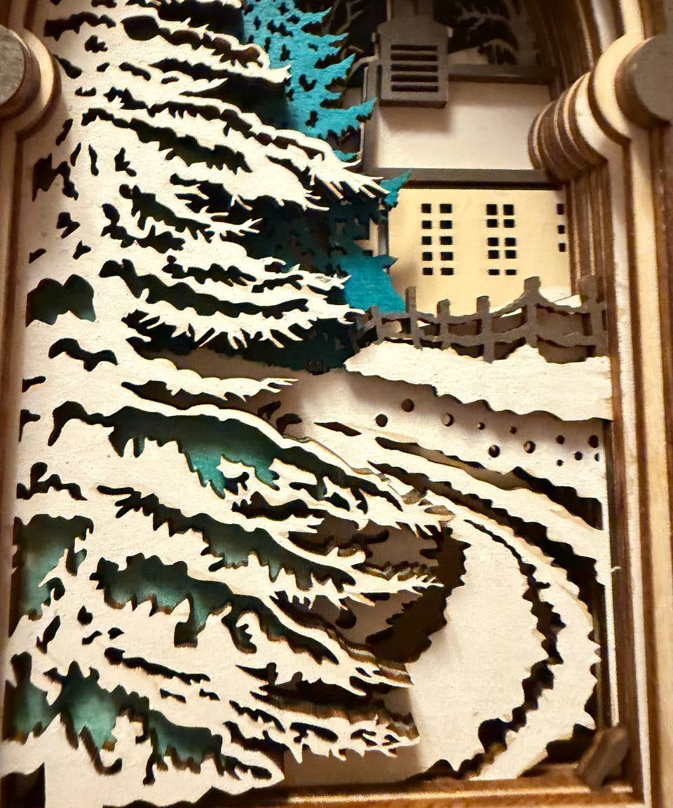 Handmade wooden Christmas book nook featuring a layered winter church, snow-covered evergreen trees and moonlit landscape for rustic Christmas bookshelf decor.