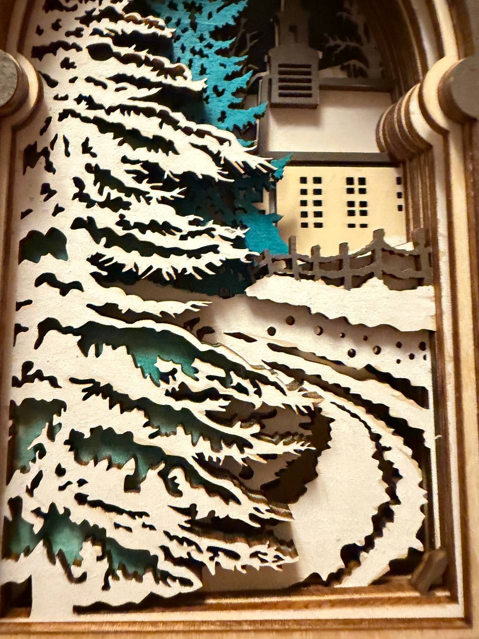 Handmade wooden Christmas book nook featuring a layered winter church, snow-covered evergreen trees and moonlit landscape for rustic Christmas bookshelf decor.