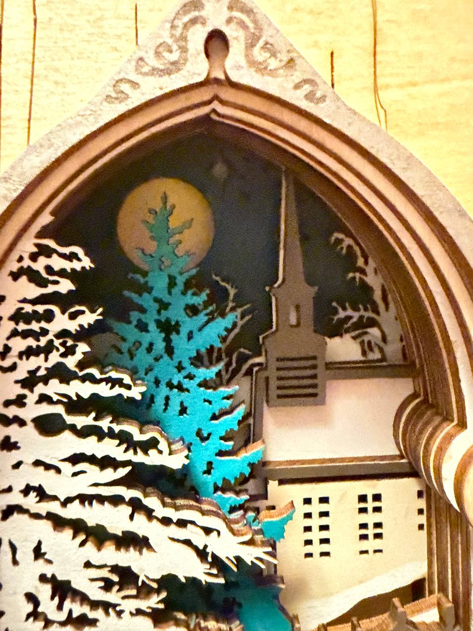 Handmade wooden Christmas book nook featuring a layered winter church, snow-covered evergreen trees and moonlit landscape for rustic Christmas bookshelf decor.