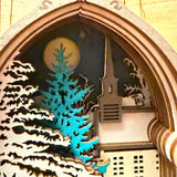 Handmade wooden Christmas book nook featuring a layered winter church, snow-covered evergreen trees and moonlit landscape for rustic Christmas bookshelf decor.