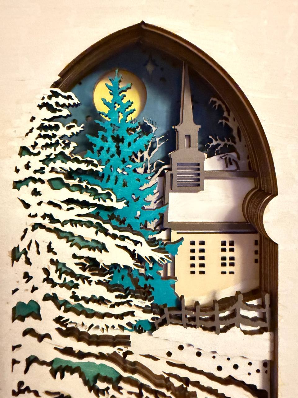 Handmade wooden Christmas book nook featuring a layered winter church, snow-covered evergreen trees and moonlit landscape for rustic Christmas bookshelf decor.