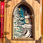 Handmade wooden Christmas book nook featuring a layered winter church, snow-covered evergreen trees and moonlit landscape for rustic Christmas bookshelf decor.