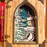 Handmade wooden Christmas book nook featuring a layered winter church, snow-covered evergreen trees and moonlit landscape for rustic Christmas bookshelf decor.
