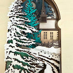 Handmade wooden Christmas book nook featuring a layered winter church, snow-covered evergreen trees and moonlit landscape for rustic Christmas bookshelf decor.