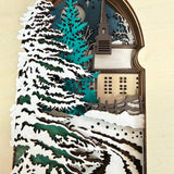Handmade wooden Christmas book nook featuring a layered winter church, snow-covered evergreen trees and moonlit landscape for rustic Christmas bookshelf decor.